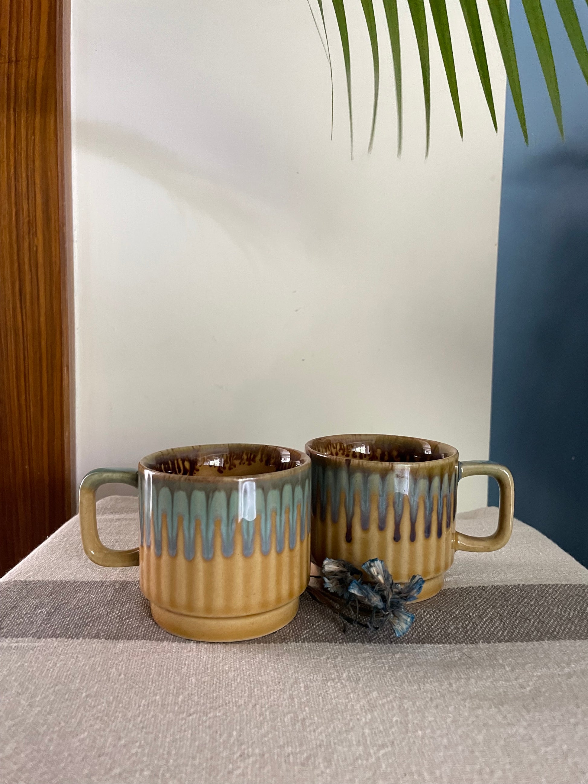Pair of short small cups with handle: mustard and grey drop glaze, brown glaze detailing inside, with dried flowers. Explore OYP's online ceramics store India