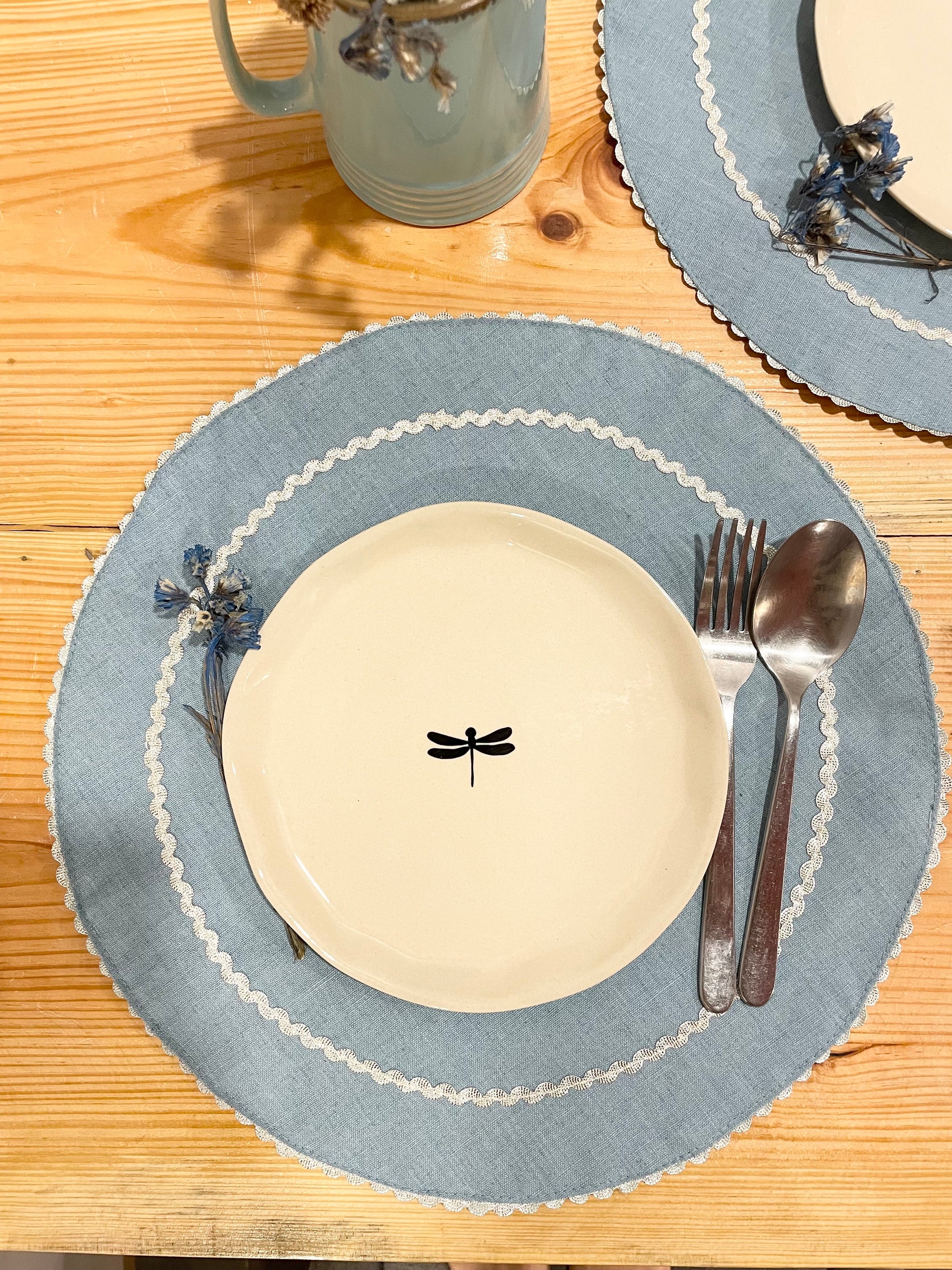 Light blue cotton table mats with zari scallop border, round ceramic plate, dried flowers, and cutlery. Buy home decor gifts India.