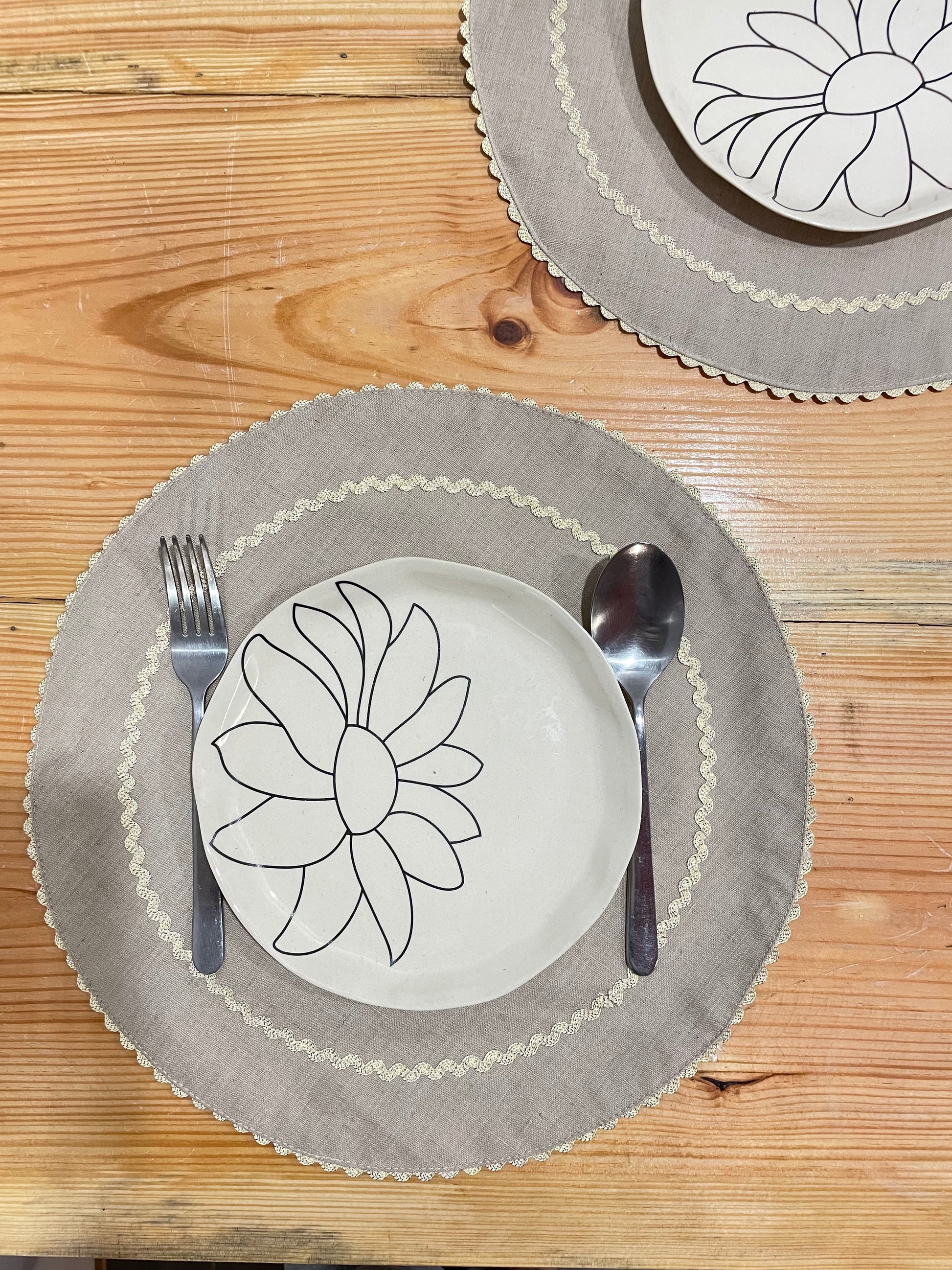 Two round beige cotton table mats with silver scallop border and interior circle, round ceramic plate, and cutlery. Buy artistic ceramics Bangalore.