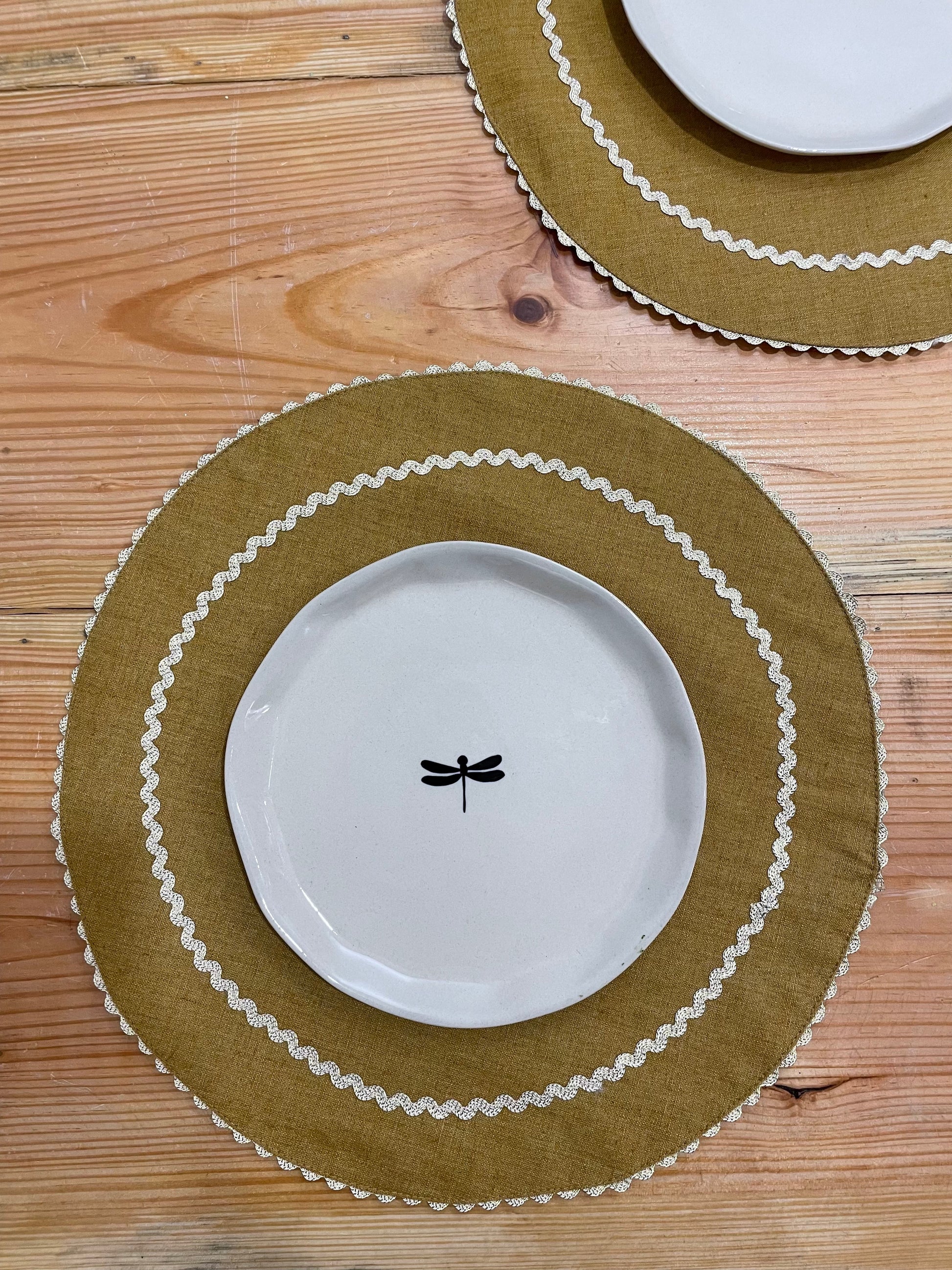 Two round olive table mats with gold scallop lace at the rim and interior circle, paired with a round ceramic plate. Buy home decor items India