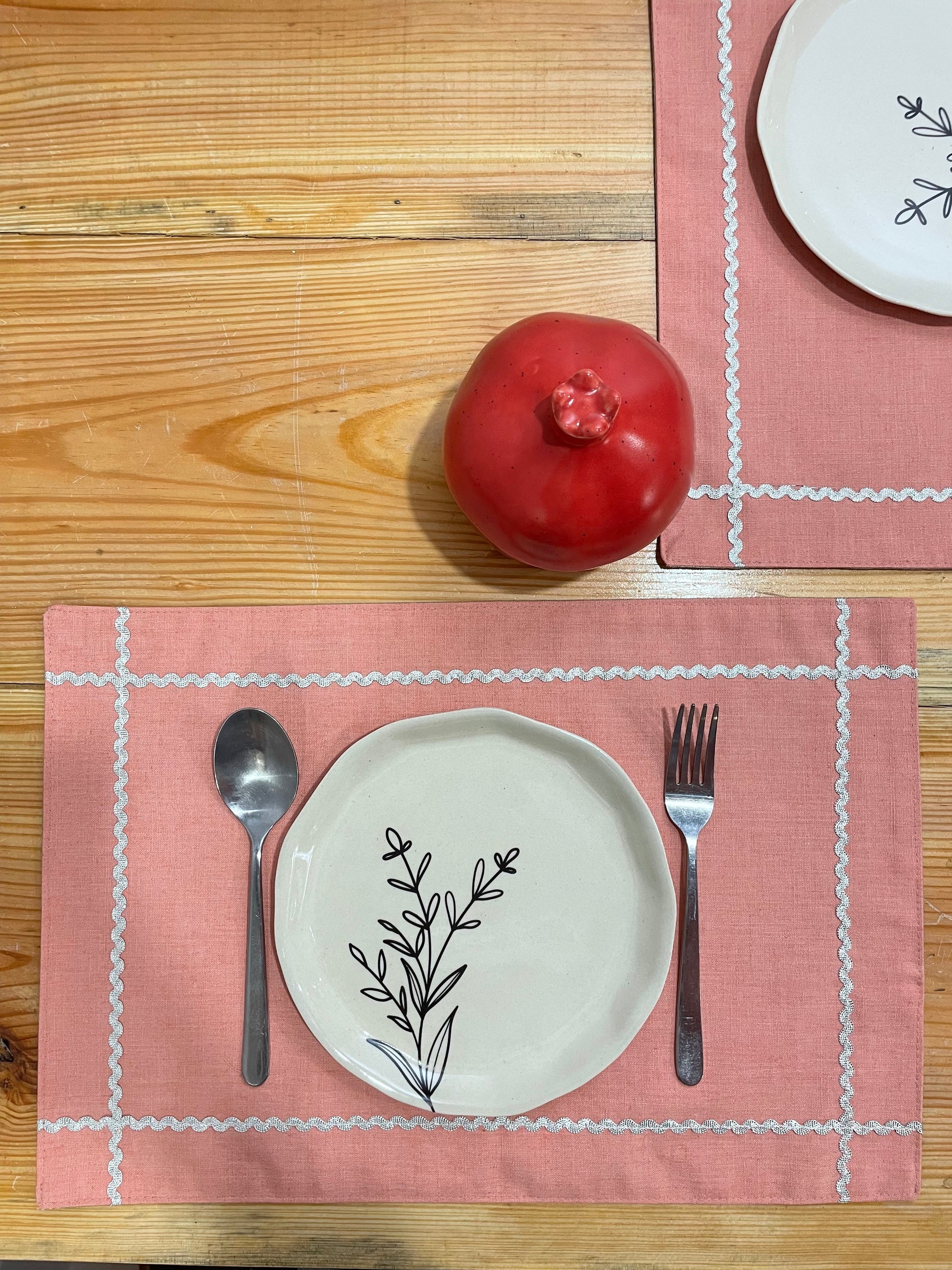 2 pink rectangle mats with silver scallop lace creating check at corners, plate, cutlery, red pomegranate jar. Explore tableware trends 2024