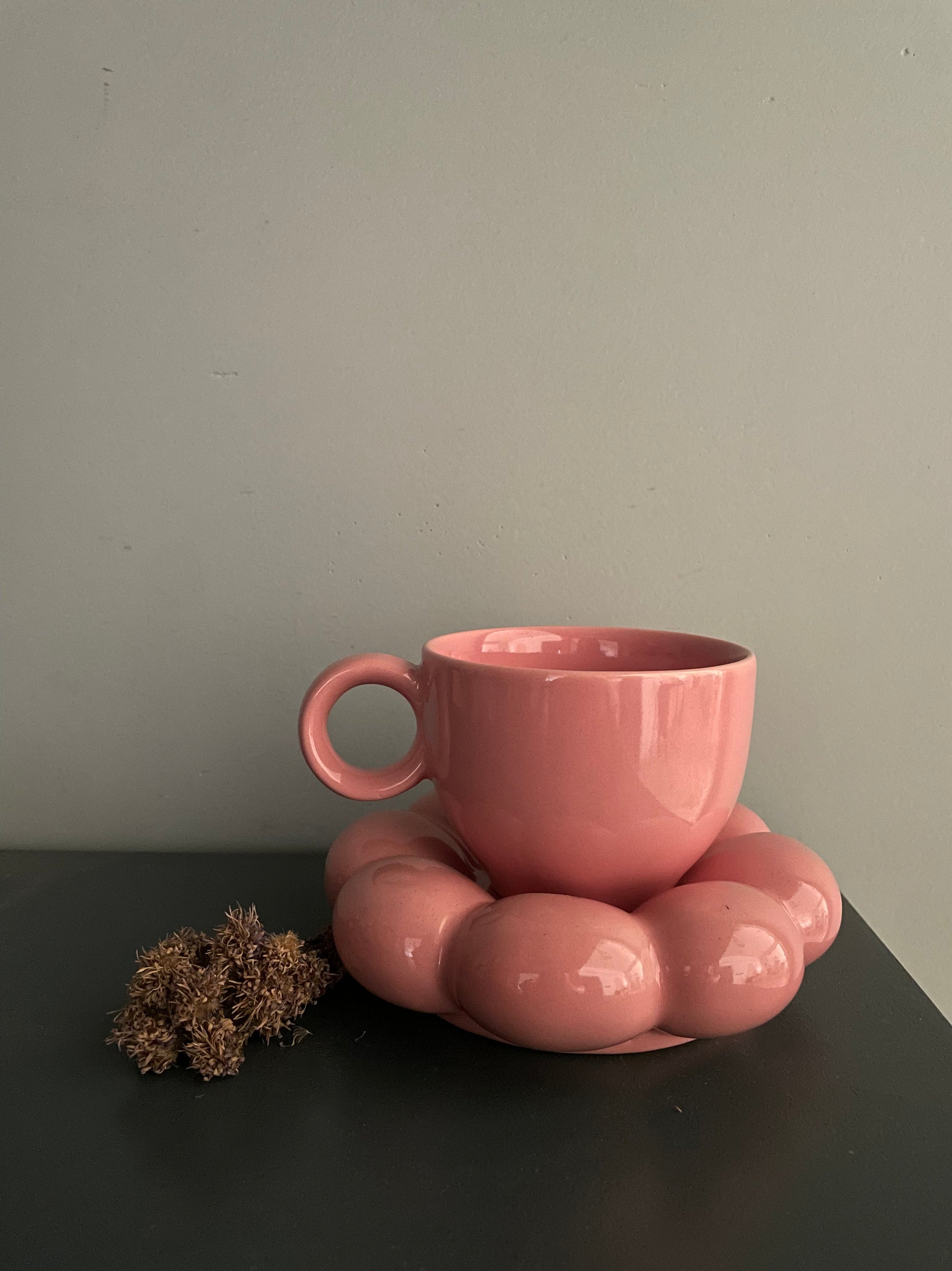 A set of pink cup & saucer: short cup with round handle, bulky cloud-like saucer, on green table with dried flowers. Buy tableware for special occasion India.