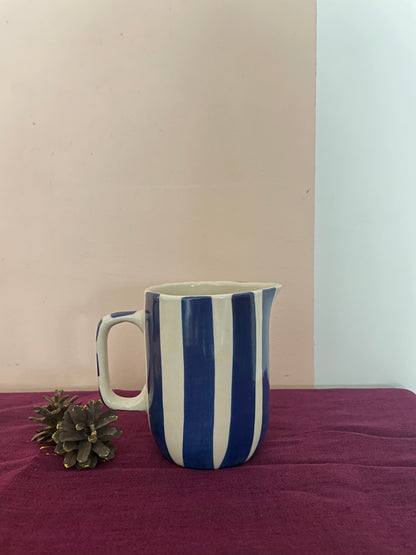 Small off-white ceramic jug with handle, hand-painted broad blue stripes on purple cloth with pine cones. Buy tableware online in India.