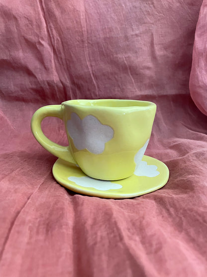 Yellow cup & saucer with off-white cloud motifs in stoneware finish on maroon cloth. Shop handcrafted ceramics India.