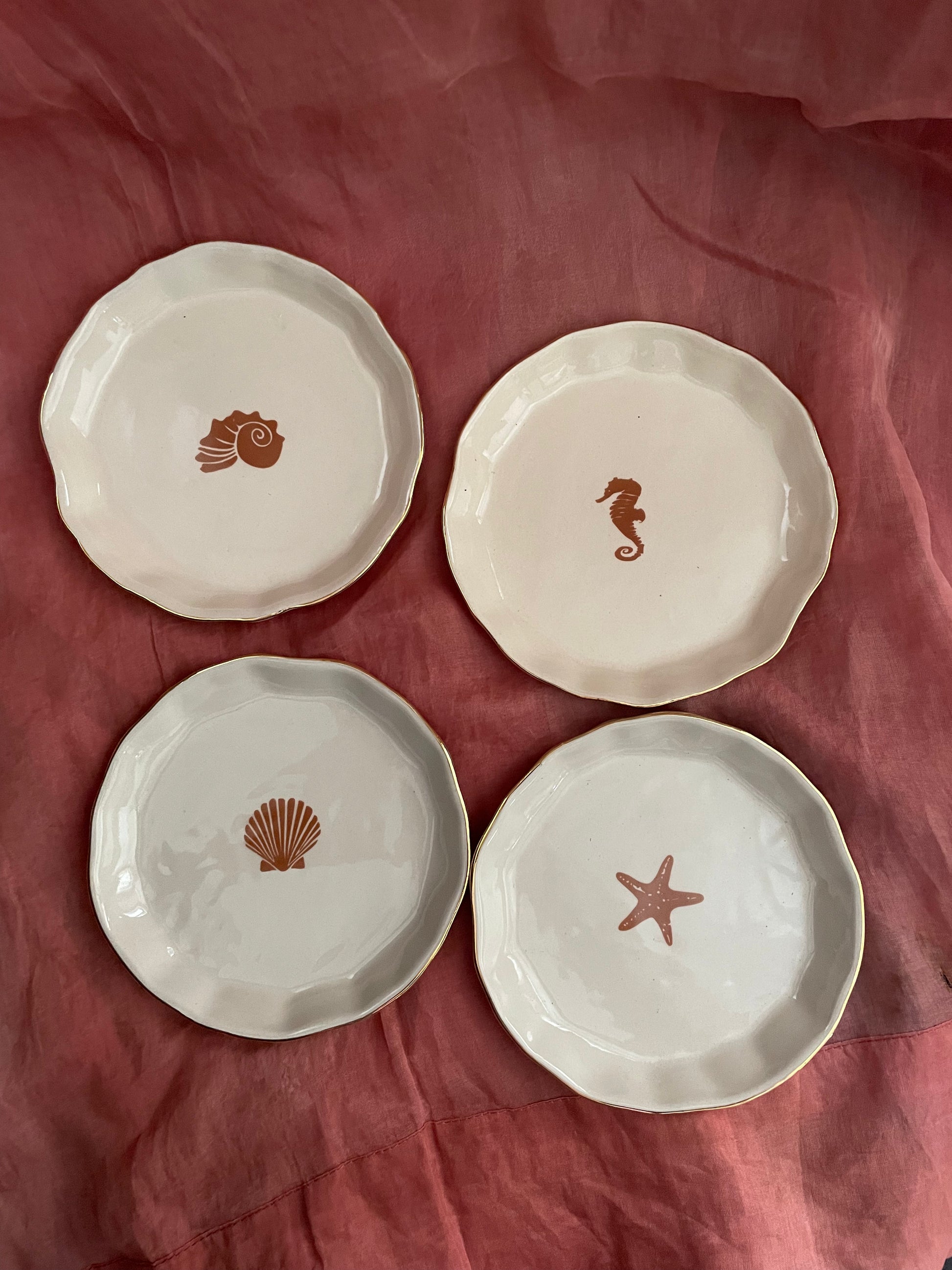 Set of 4 small off-white ceramic plates, each with a unique orange motif, placed on orange cloth. Buy kitchenware in Bangalore.