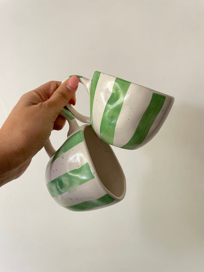 Hand holding out pair of short off-white ceramic cups with hand-painted green stripes and freckle detailing. Buy tableware online in Bangalore.