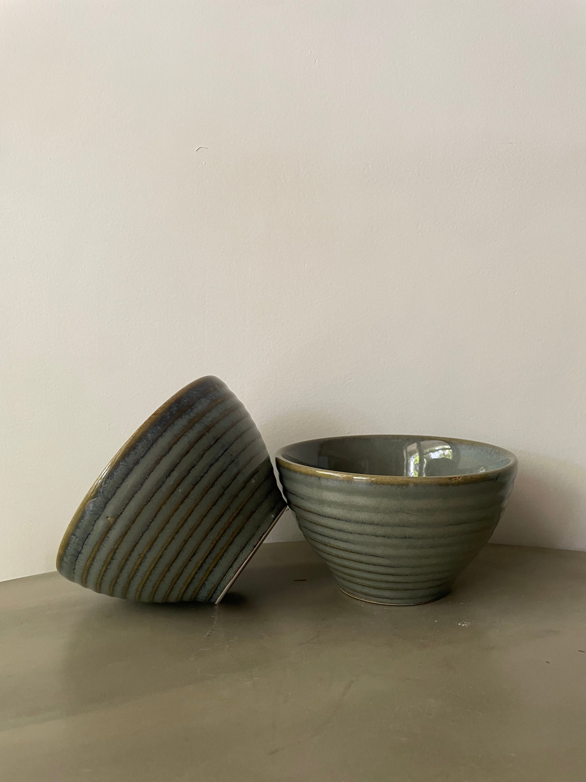 Pair of medium deep bowls in subtle green glaze, one tilted on the other. Shop traditional Indian ceramics.