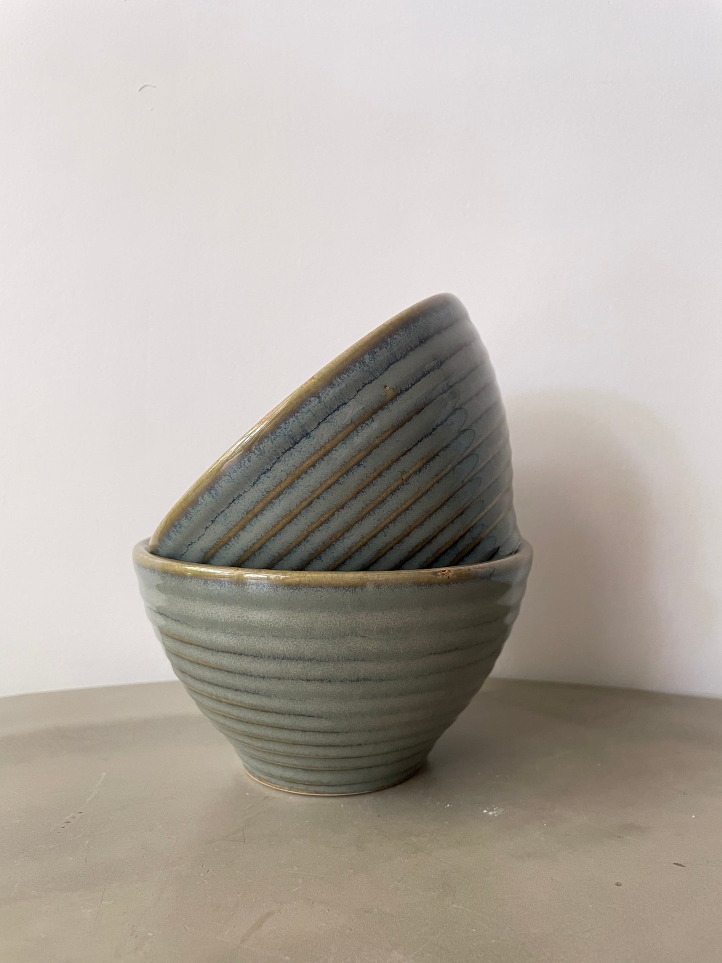 Pair of deep, medium green glazed ribbed ceramic bowls stacked on table. Shop affordable ceramics in Bangalore.