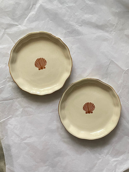 Set of 2 small uneven off-white ceramic plate with orange sea shell motif and gold rim on white paper. Buy affordable ceramics in India.