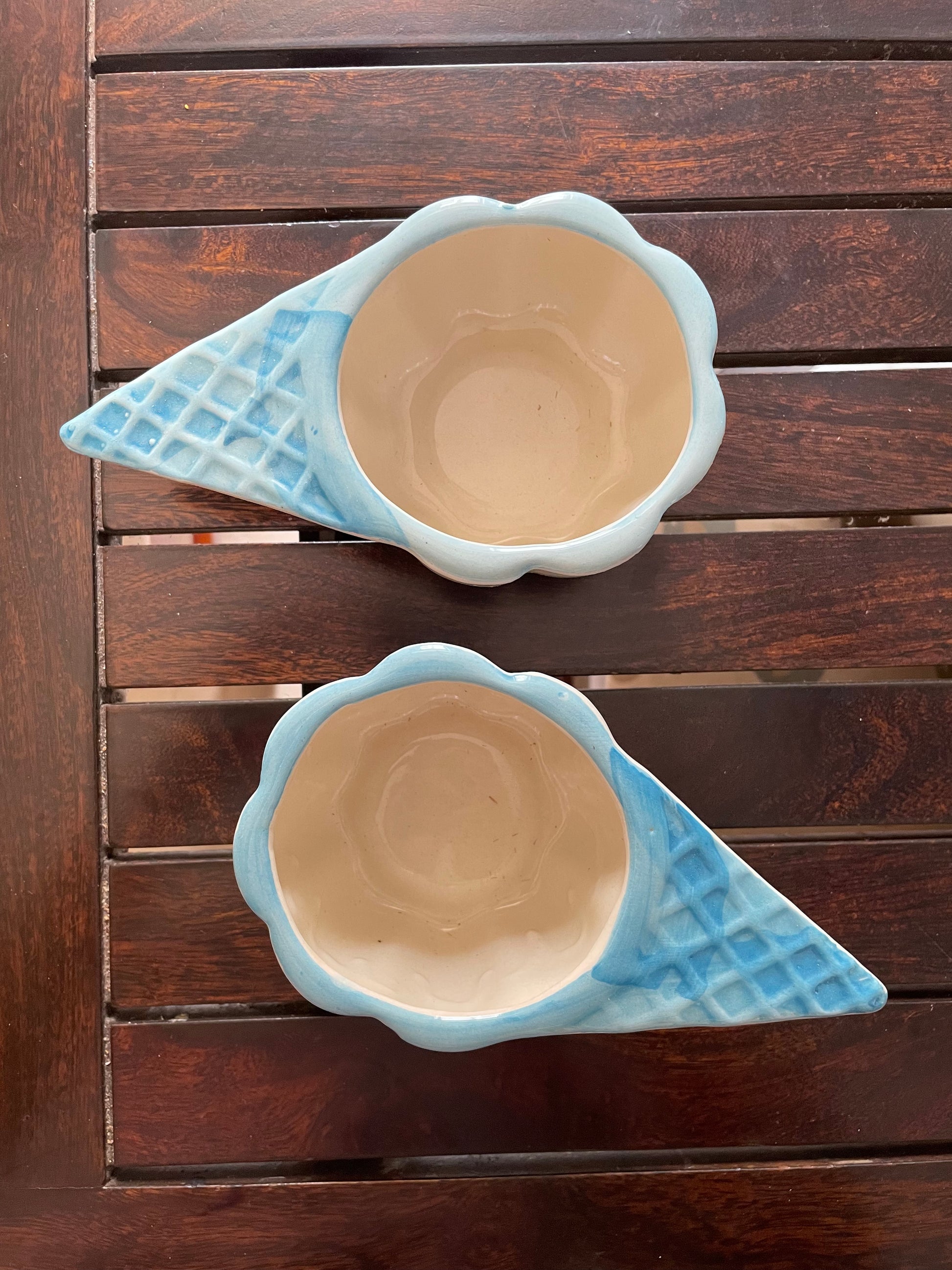 Set of 2 light blue ceramic ice cream cone-shaped bowls on wooden table. Waffle cone handle, scallop rim. Explore unique gifting ideas in Bangalore.