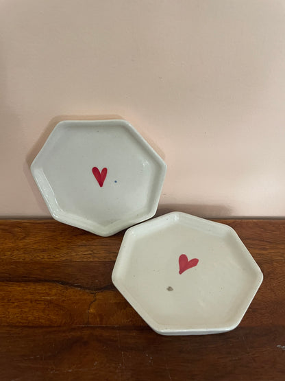 Set of 2 hexagon off-white coasters with hand-painted red heart, one against a pink wall and the other flat on a wooden table. Shop kitchenware Bangalore.