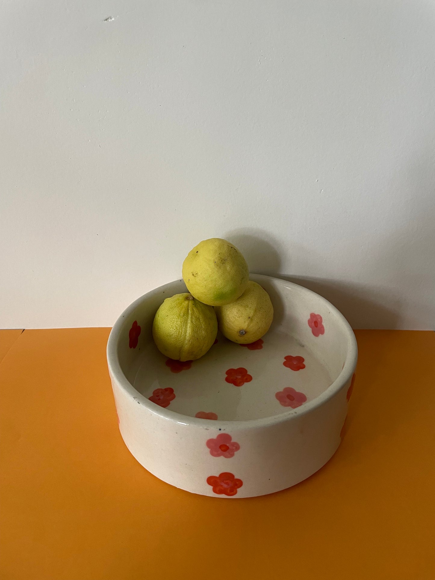 Medium round ceramic bowl with hand painted red & orange flowers with lemons placed inside. shop home decor gifts India