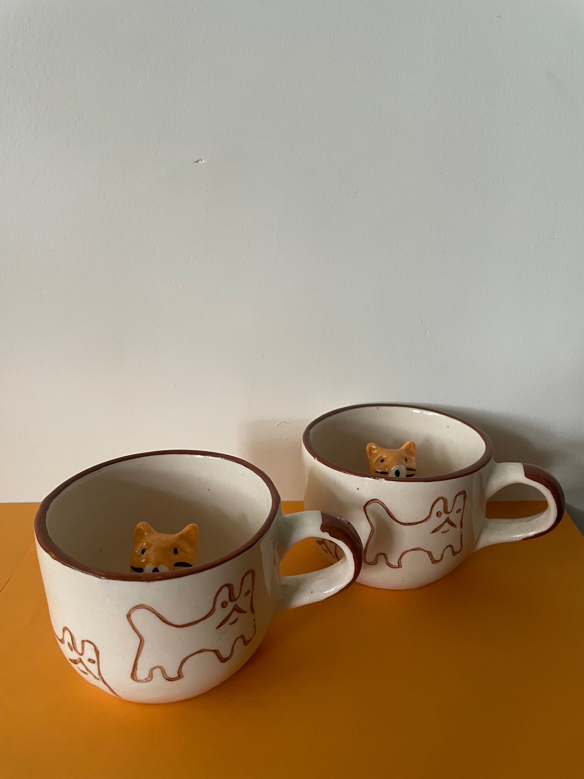 Medium ceramic cups, brown handle, cat outline drawn outside and peek a boo cat figure inside mug. Shop handmade mugs India