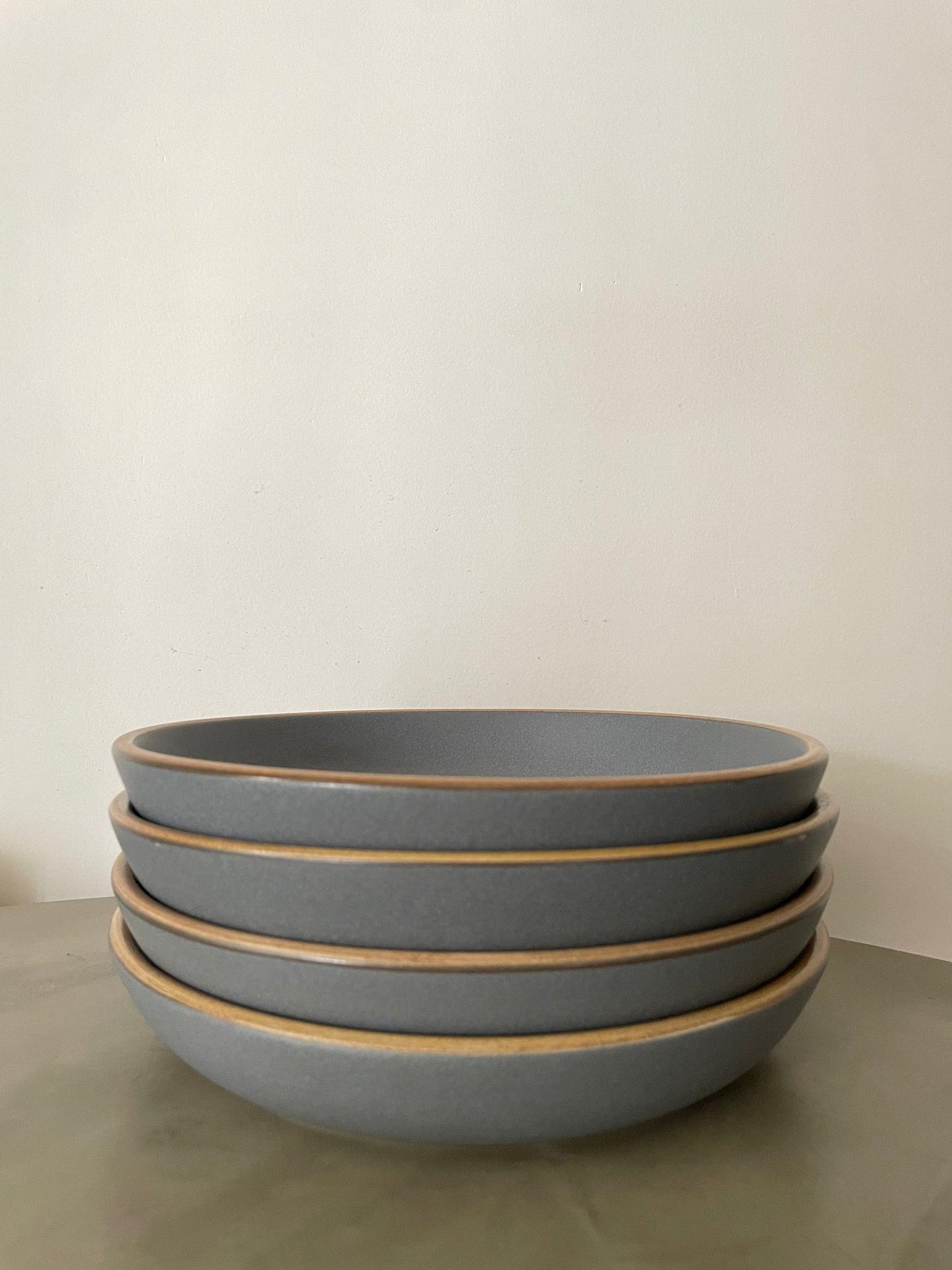 Stack of 4 large round ceramic plates in grey stoneware finish with mustard rims on a cement table. Buy affordable ceramics Bangalore.