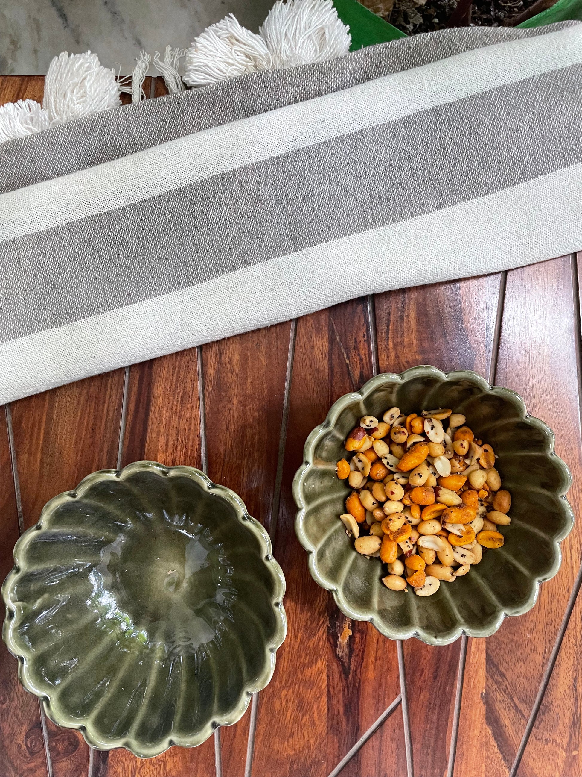 flower-shaped rim, deep green glaze katori bowls; one filled with snack, other empty in outdoor setting. Explore designer tableware in Bangalore.