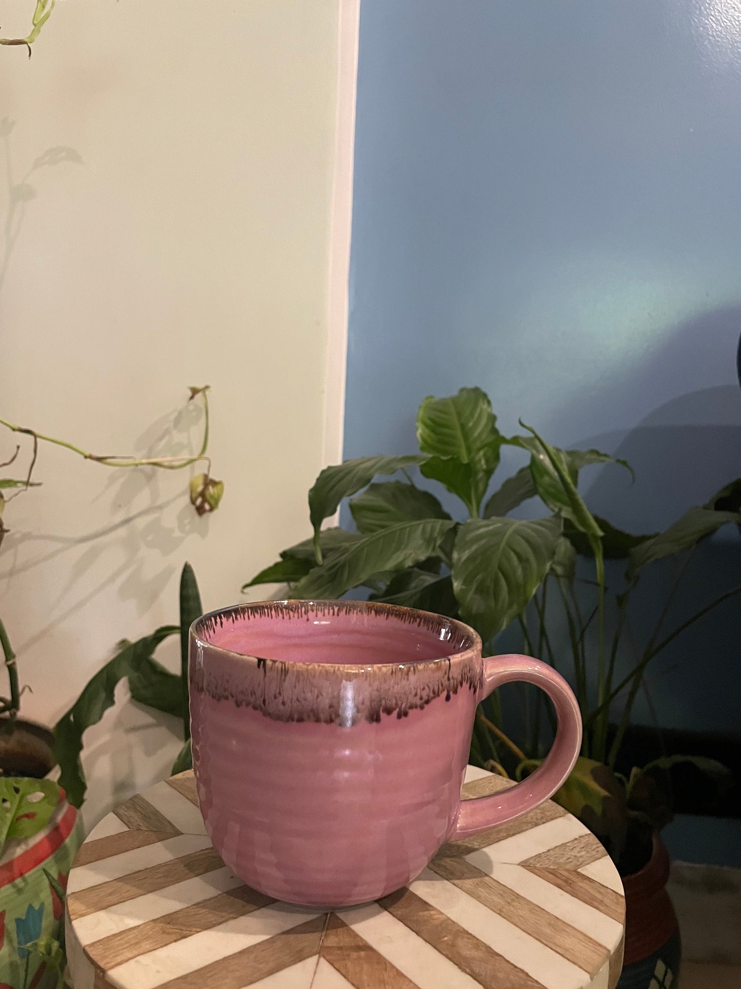 Large pink glaze ceramic rounded mug with brown drip detailing, on round chevron designed table with plants. Buy luxury ceramics Bangalore.