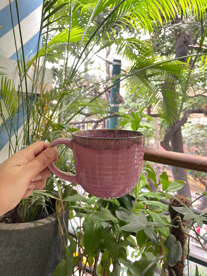 Hand holding large pink rounded ceramic mug with handle on balcony, greenery in background. Buy kitchenware Bangalore