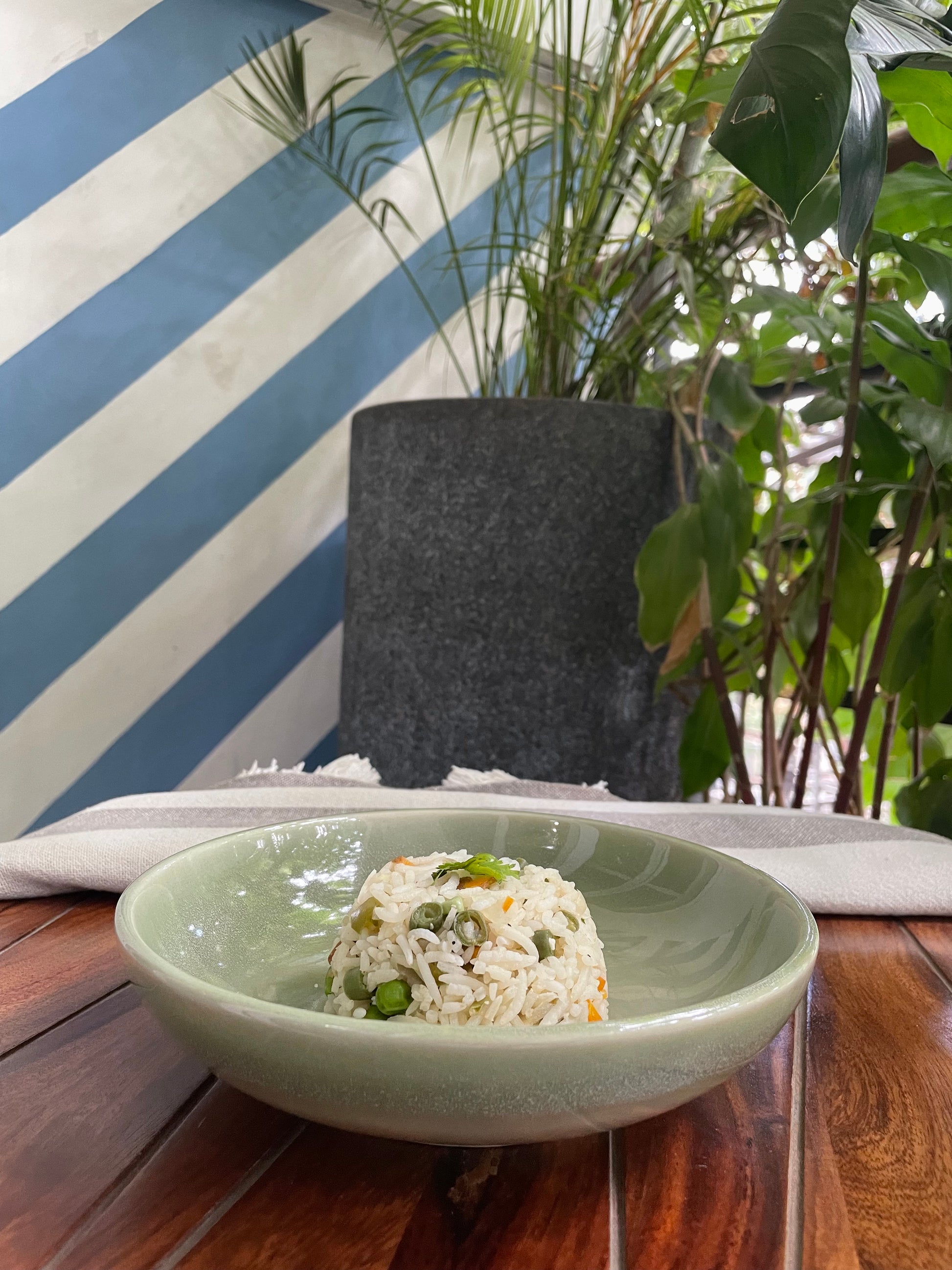 A pastel green glazed shallow ceramic bowl on outdoor table filled with rice. Buy tableware for special occasions in India.