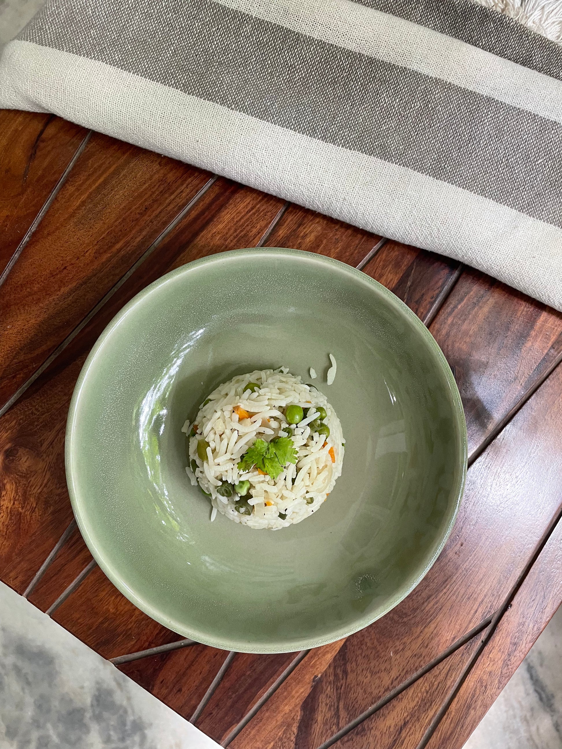 Top view of green glazed ceramic bowl with tonal shades, filled with rice on wooden table. Explore ceramics in India.