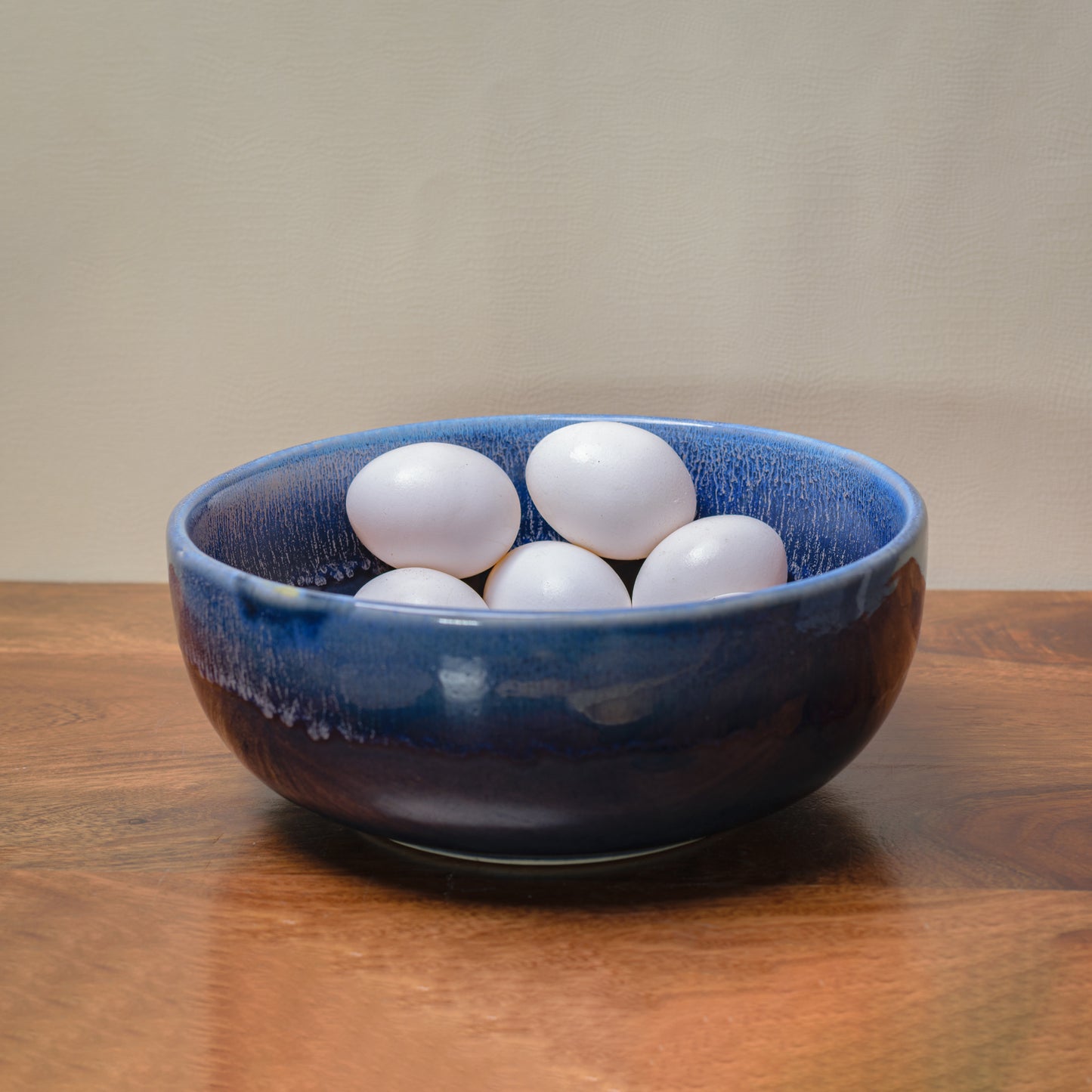 A large ceramic bowl with shades of blue glaze inside and out, eggs inside. Shop artistic ceramics in India.