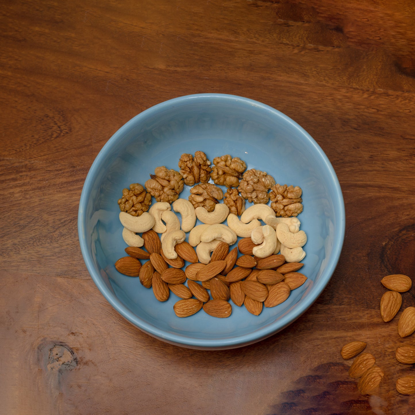 Top view of sky blue ceramic bowl filled with dry fruits on wooden table. Buy designer tableware in Bangalore.