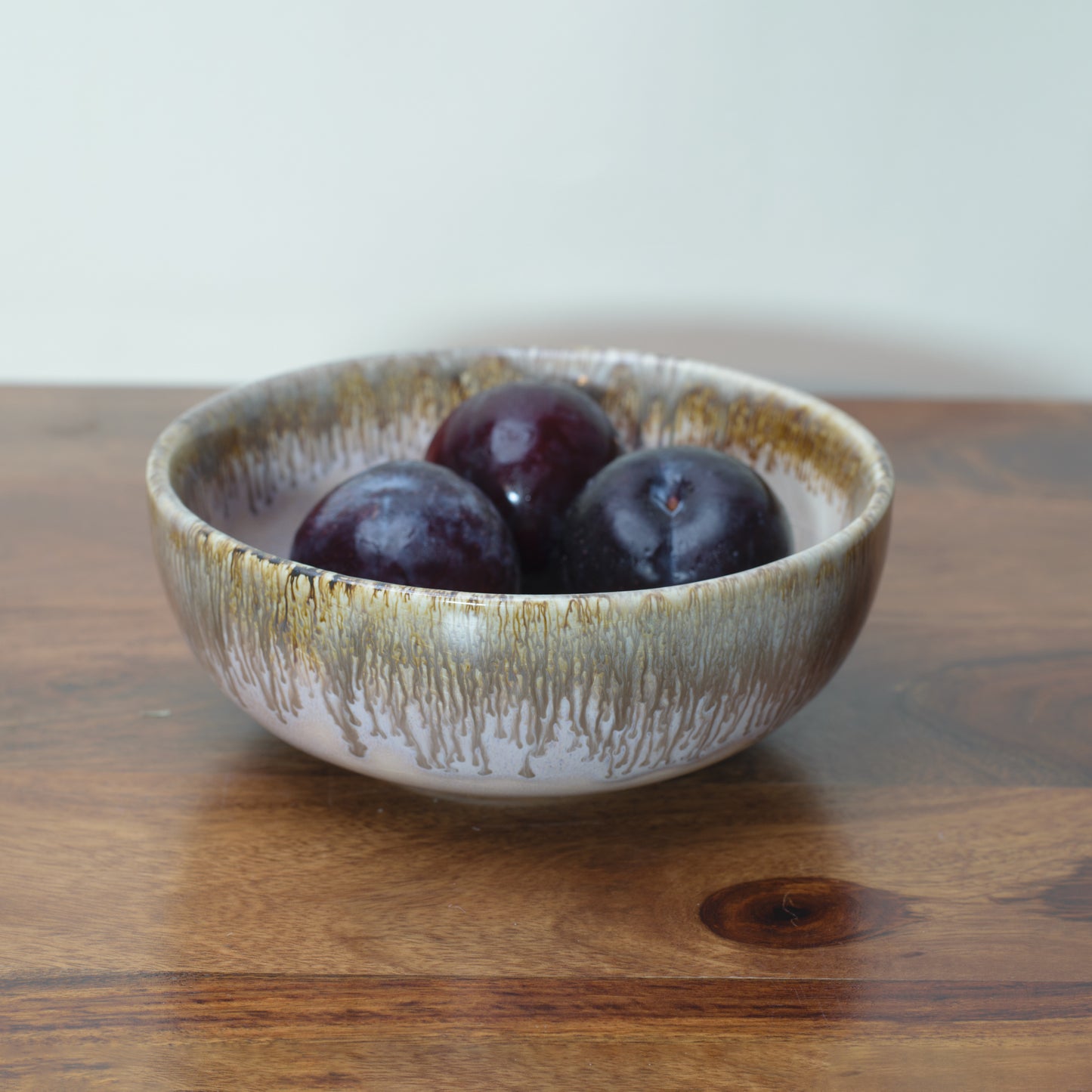 Small ceramic bowl, light pink glaze with brown drip from rim, plums inside. Discover home decor gifts in India.