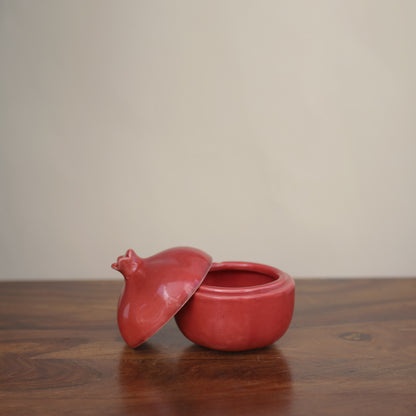 A medium red pomegranate-shaped jar with open lid on wooden table. Buy tableware online Bangalore.