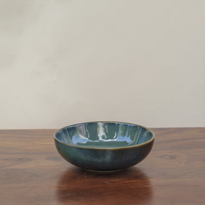 A green glazed ceramic bowl, elegant and earthy, on a wooden table with different glaze tones. Buy traditional Indian ceramics.