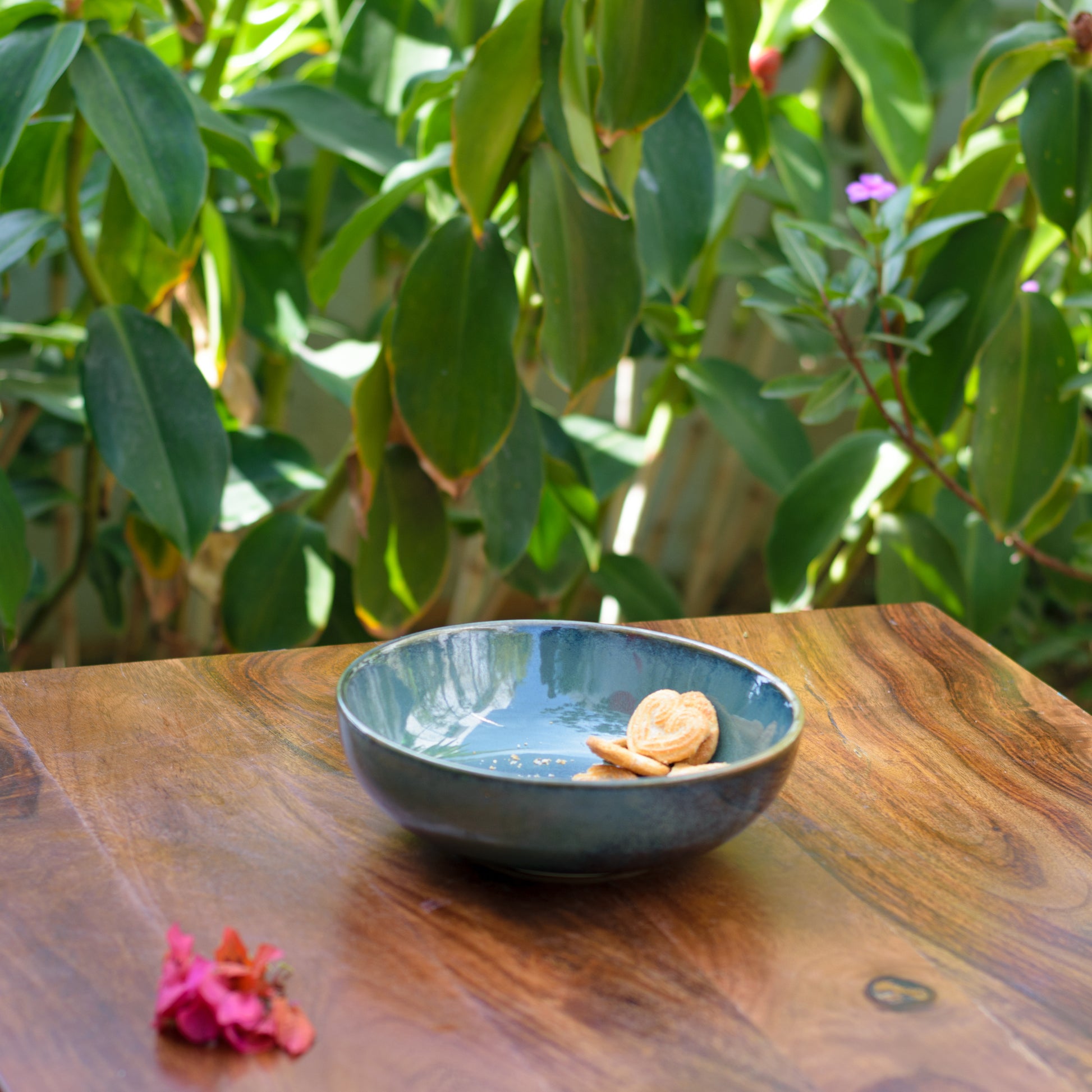 A ceramic bowl with tones of green glaze and a few biscuits on a table in an outdoor setting. Elegant and must-have. Shop gifting items in Bangalore.